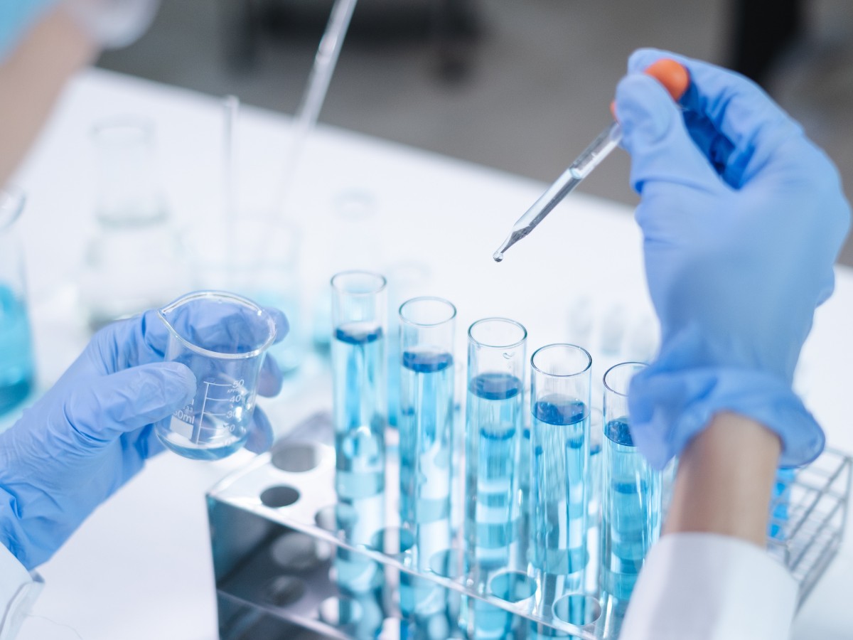 Gloved hands using a dropper over test tubes in a laboratory
