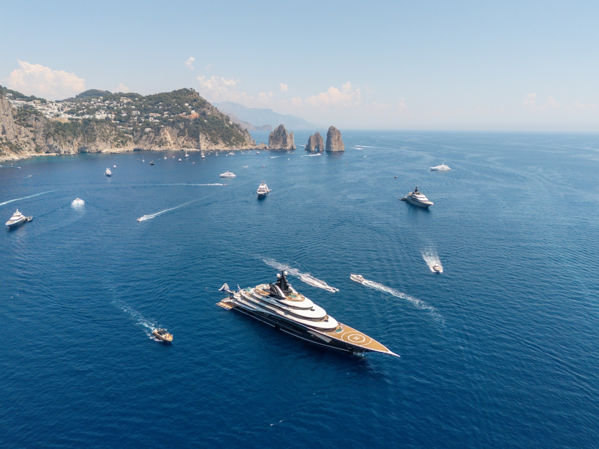 Superyacht with a helipad at anchor in a blue bay, surrounded by smaller boats