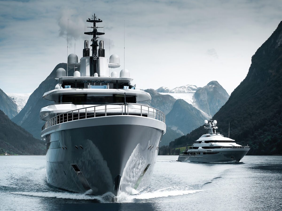 Superyacht heading towards the camera in a mountain fjord, with a second yacht behind